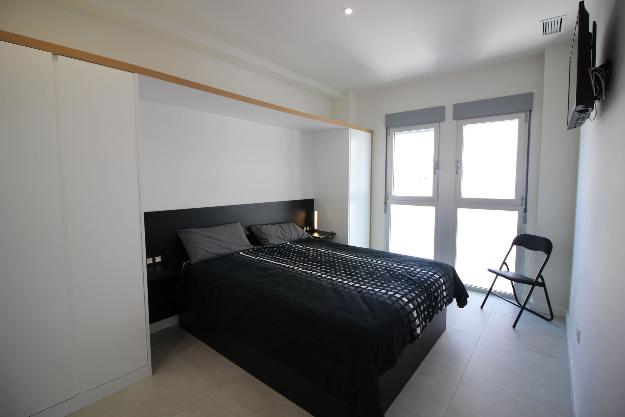 A bedroom with a bed, a chair, a TV, and a window.