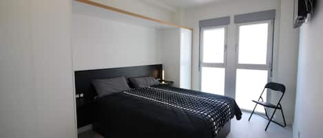 Un dormitorio con cama, una silla, televisión y ventana.