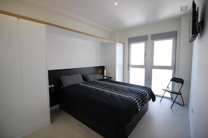 Ein Schlafzimmer mit Bett, Sessel, Fernseher und Fenster.