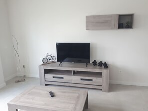 A living room with a TV on a wooden stand, a bicycle, and a few small figurines. - Apartment Mirador de Villamartin (Orihuela)
