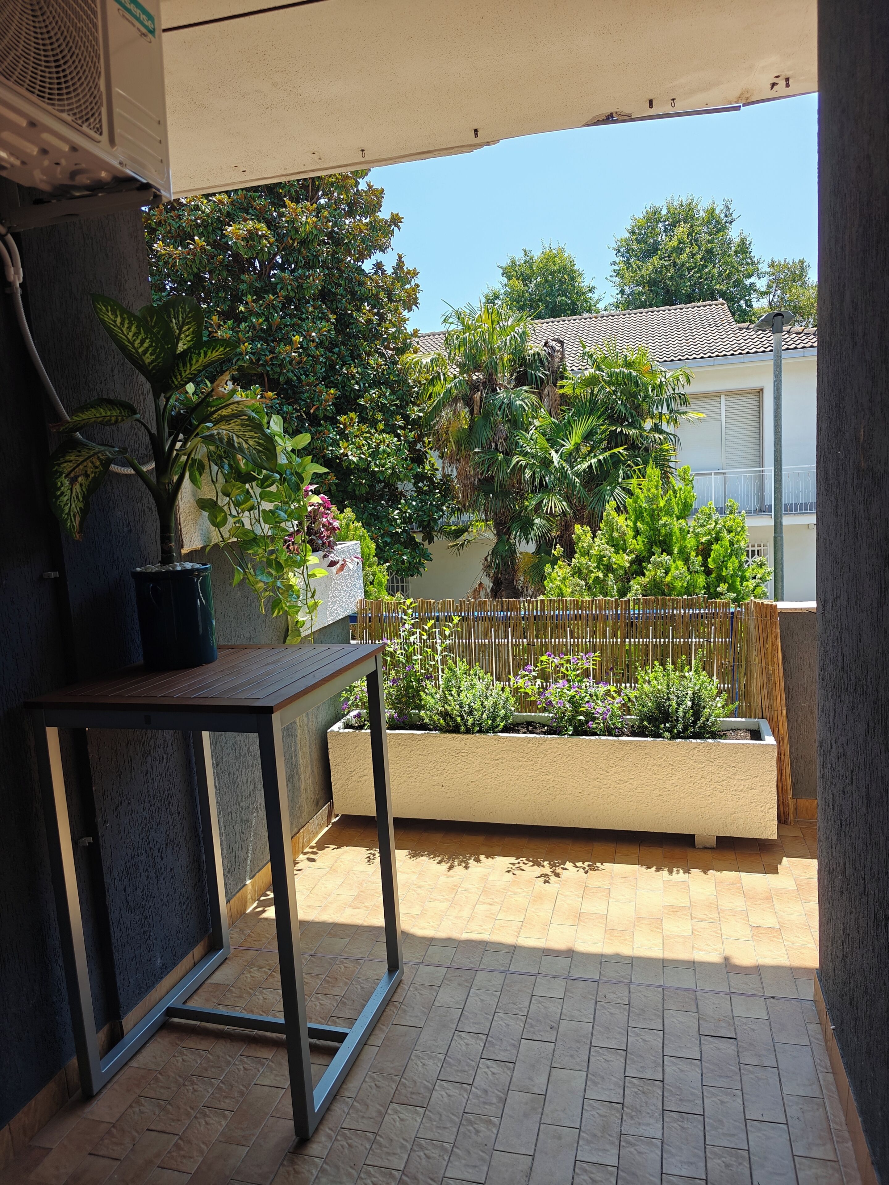 Een balkon met een tafel, planten in potten en uitzicht op een huis met een pannendak.