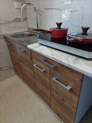 Eine Küche mit Spülbecken aus Edelstahl, Holzschränken, einer Marmor-Spritzschutzwand und einem eingebauten Induktionskochfeld.
