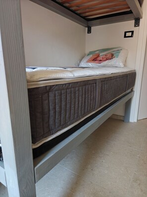 Uma cama beliche com colchão e travesseiros, teto de madeira e chão de azulejos.