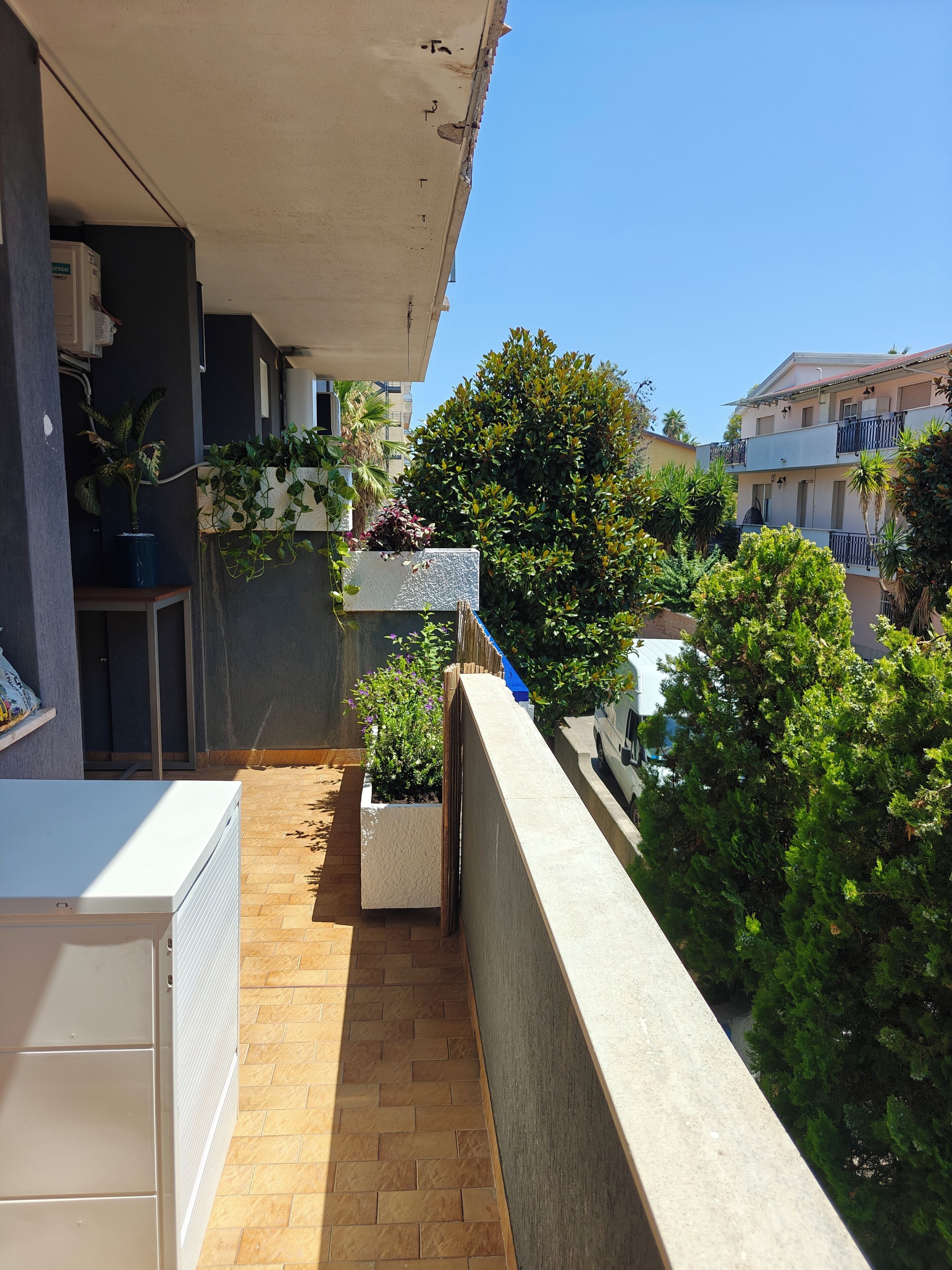A balcony with a tiled floor, potted plants, and a white appliance.