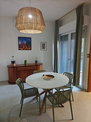 A dining area with a round table, four chairs, a hanging light fixture, a cabinet, and two framed artworks. - New apartment 100 m from the sea (Montesilvano)
