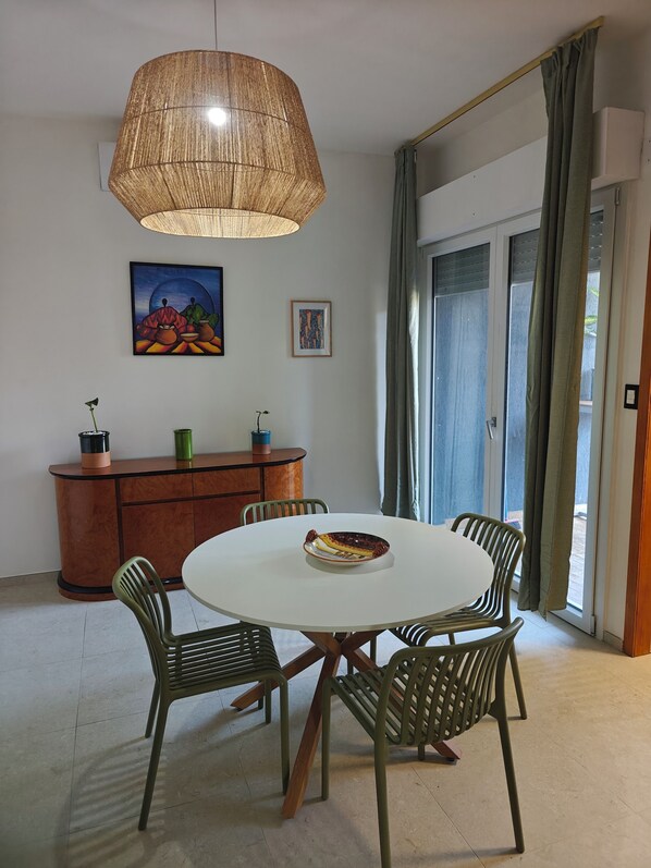 Uma sala de jantar com mesa redonda, quatro cadeiras, luminária pendente, armário e duas obras de arte emolduradas.
