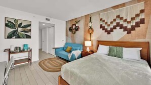 A hotel room with a bed, a sofa, a bedside table, a lamp, and a wall with a geometric pattern. - Sunset View 2BR - Resort Pool & Beach Shuttle (Hallandale Beach)