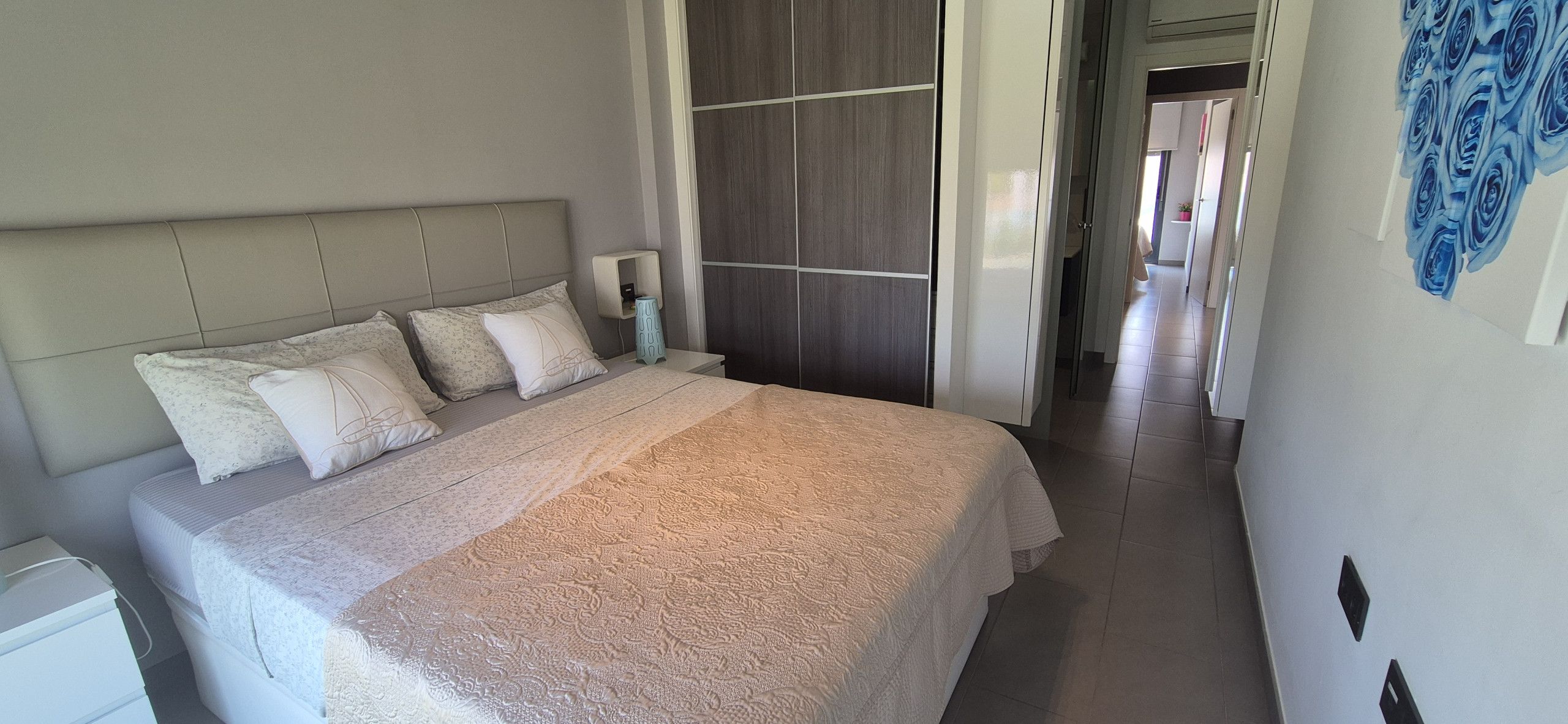 Una cama bien hecha con una colcha estampada, una mesita de noche con una lámpara y una pared con un mural floral.