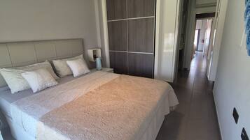 Una cama bien hecha con una colcha estampada, una mesita de noche con una lámpara y una pared con un mural floral.