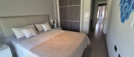 A neatly made bed with a patterned bedspread, a bedside table with a lamp, and a wall with a floral mural.