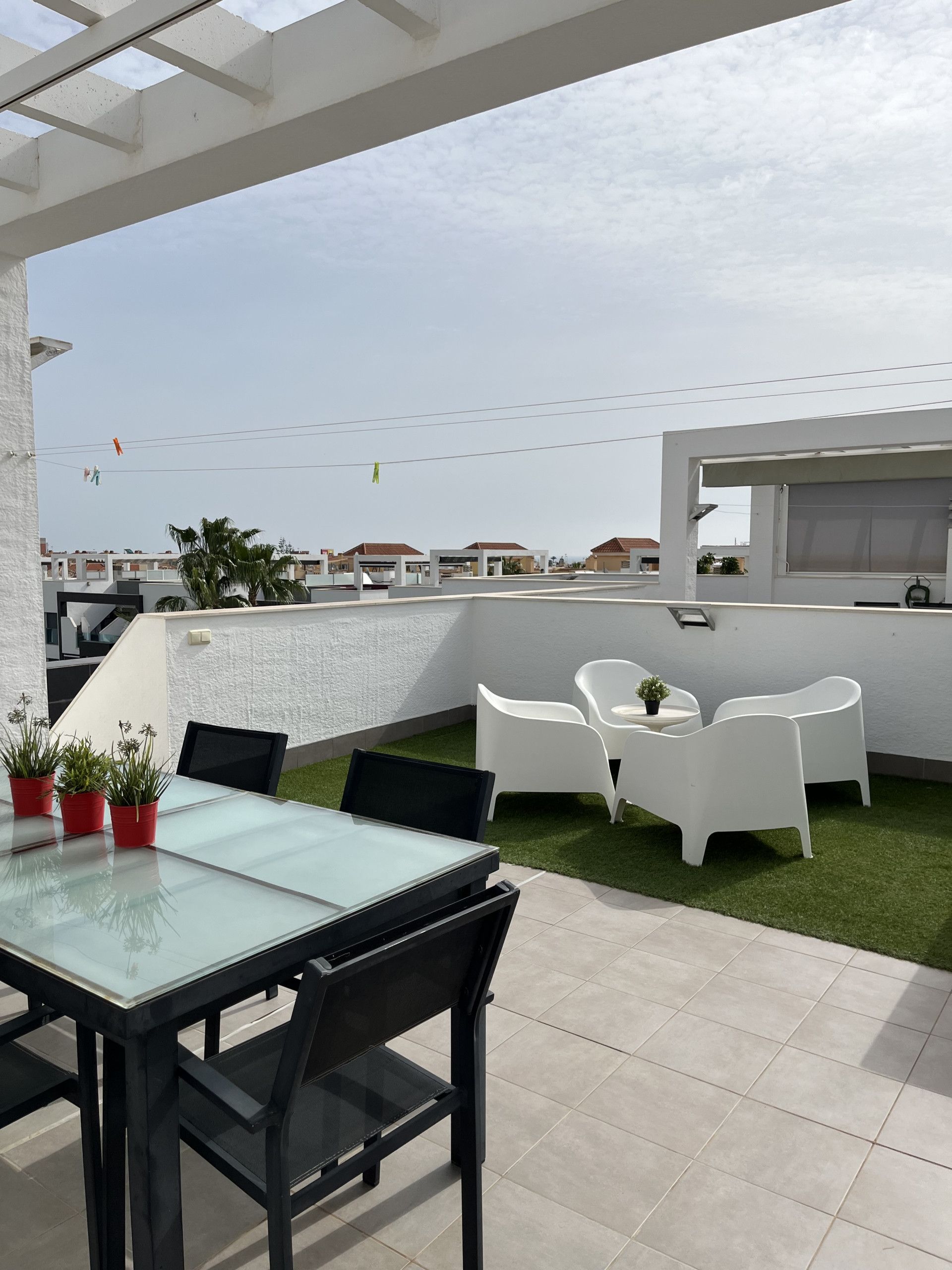 A rooftop terrace with a glass table and chairs, a small garden area with potted plants, and a view of the cityscape.
