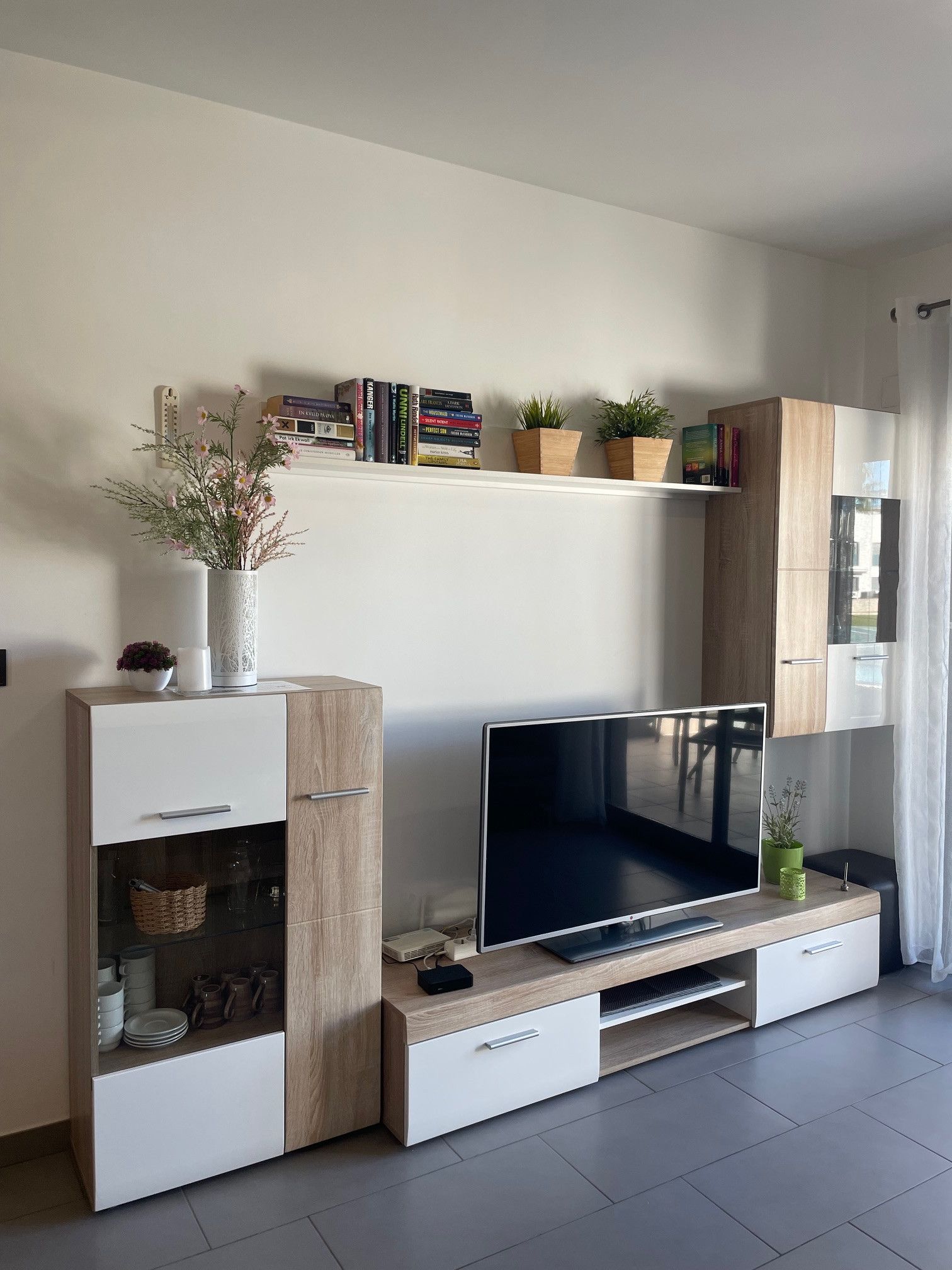 Una sala de estar moderna con un televisor de pantalla plana, armarios de madera y estantes con libros y plantas.