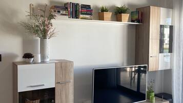Una sala de estar moderna con un televisor de pantalla plana, armarios de madera y estantes con libros y plantas.