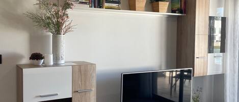 A modern living room with a flat-screen TV, wooden cabinets, and shelves with books and plants.