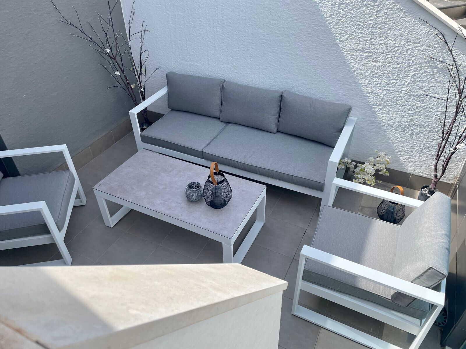A modern outdoor seating area with a grey sofa, white chairs, and a coffee table.