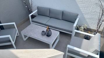 A modern outdoor seating area with a grey sofa, white chairs, and a coffee table.