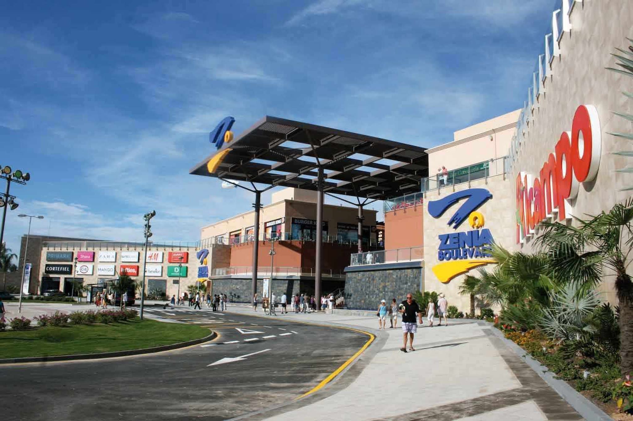 Un edificio comercial con un gran letrero que dice 'ZENIA BOULEVARD' y varias tiendas, incluyendo 'Burger King' y 'Mango'.