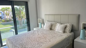 A bedroom with a large bed, a nightstand, a bedside table, and a view of a landscaped area outside.