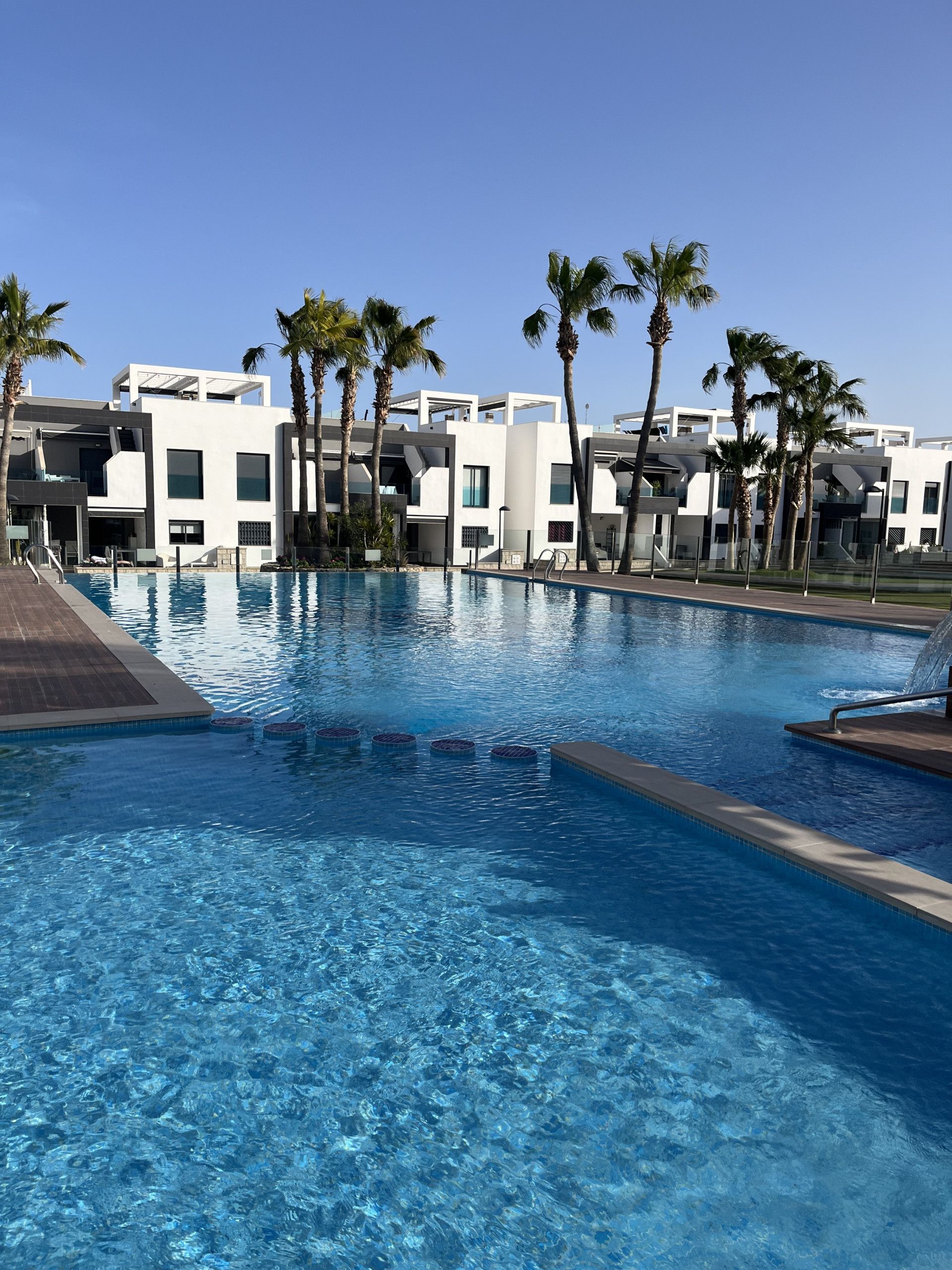 Una piscina con agua azul cristalina, rodeada de palmeras y edificios modernos.