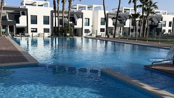 Una piscina con agua azul cristalina, rodeada de palmeras y edificios modernos.