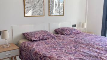 Une chambre à coucher avec un lit, deux reproductions botaniques encadrées accrochées au mur, une table de chevet avec une lampe et une commode.