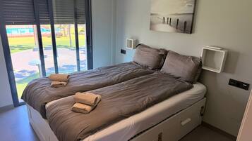 Una cama doble con vistas a una piscina y un jardín, a través de un ventanal corredero.