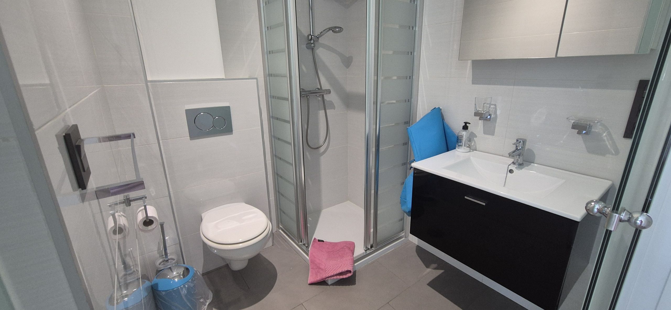 Une salle de bain moderne dotée d’une douche à parois de verre, de toilettes et d’un lavabo avec un meuble noir.