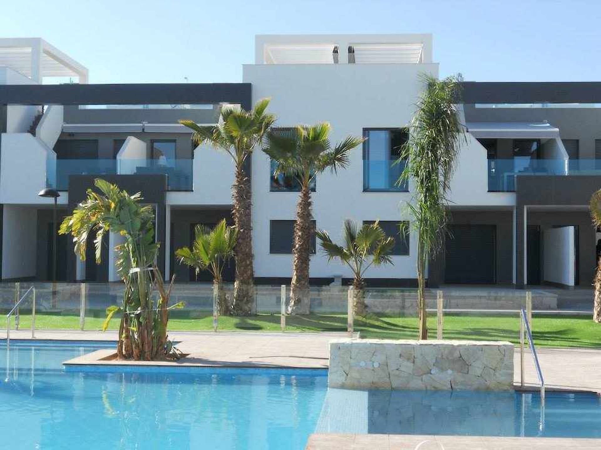 Een modern hotel met een zwembad, palmbomen en een verzorgd gazon.