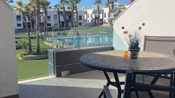 A balcony with a view of a swimming pool, palm trees, and modern buildings.