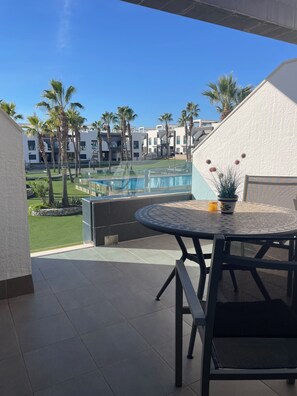 A balcony with a view of a swimming pool, palm trees, and modern buildings.