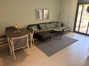 A modern living room with a dining table, sofa, and ottoman. There are two framed pictures on the wall and a floor lamp. - Penthouse Oasis Beach II la Zenia (Orihuela)