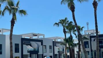 A modern pool area with clear blue water, surrounded by palm trees and contemporary buildings.