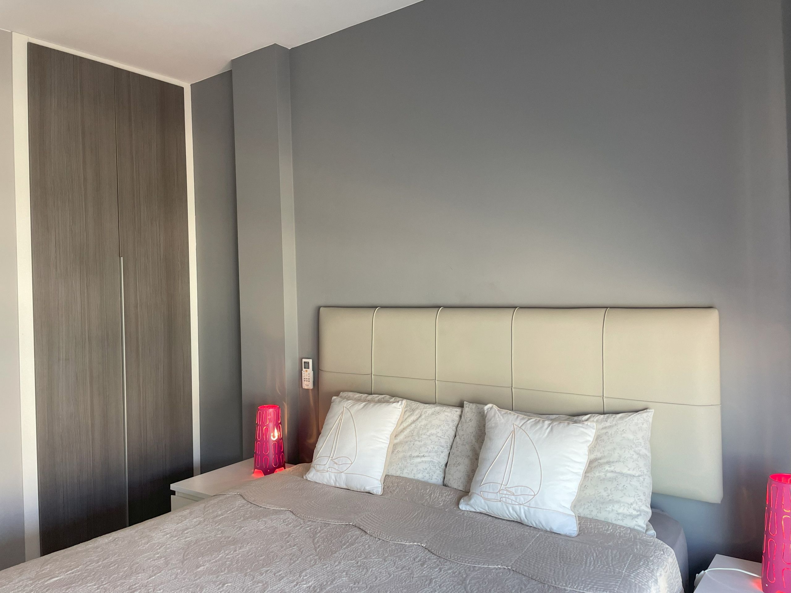 Une chambre à coucher avec un lit, une table de chevet, une lampe rouge et une armoire grise.