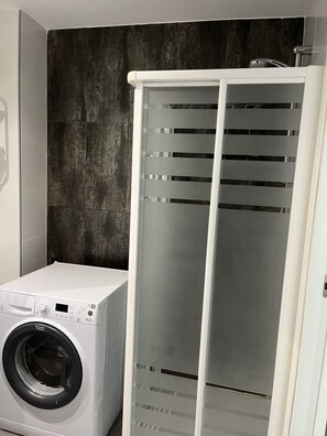 A laundry room with a front-loading washing machine, a drying rack, and a dark textured wall.