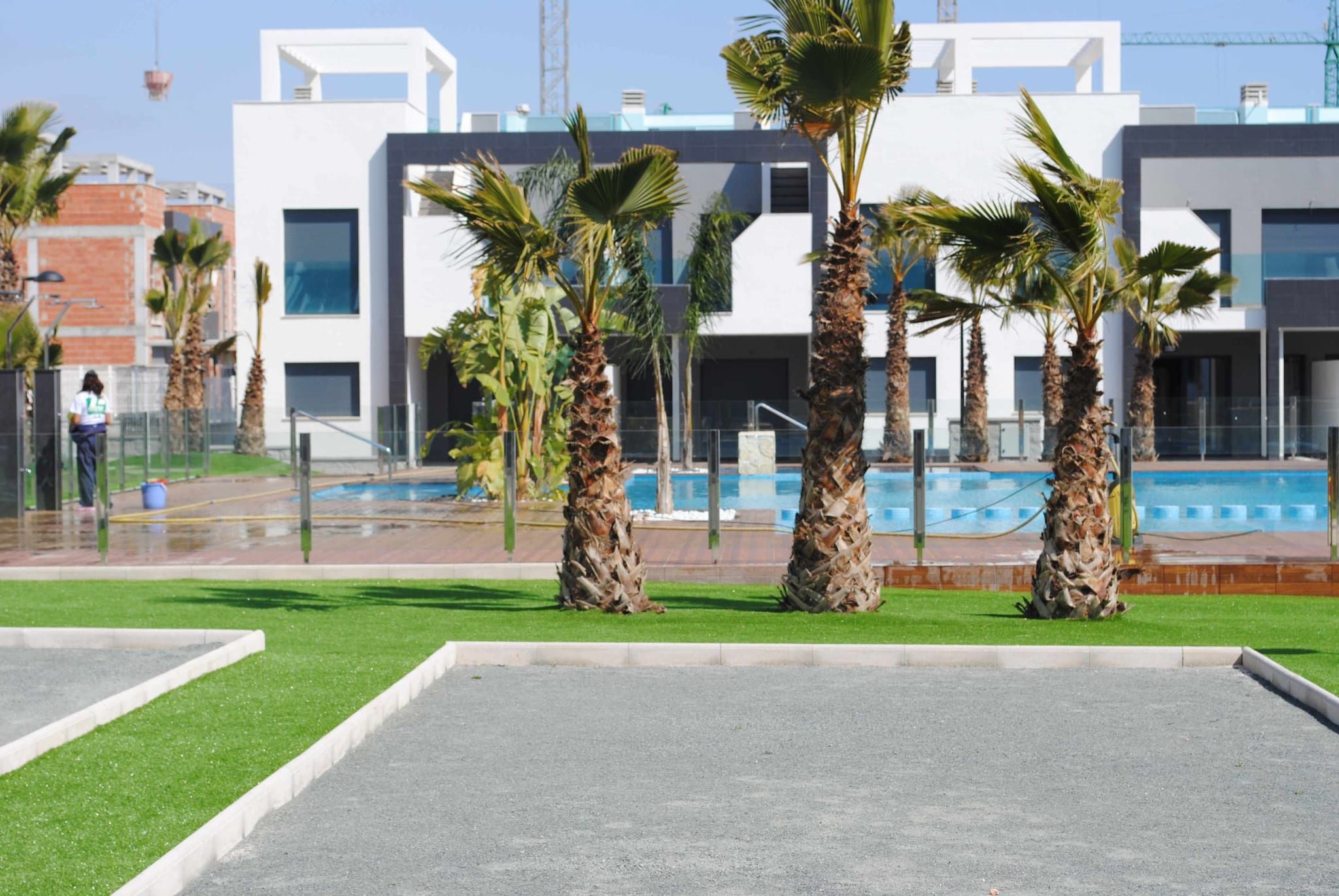 A modern building with a swimming pool, palm trees, and a person walking in the background.