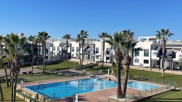 Un área de piscina con dos piscinas rectangulares, rodeada de palmeras y un césped bien cuidado.
