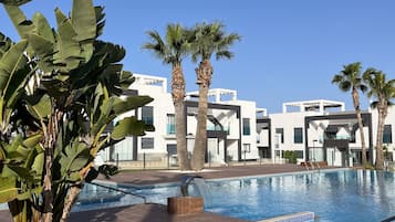 A swimming pool with a modern design, surrounded by palm trees and a building with a contemporary architectural style.