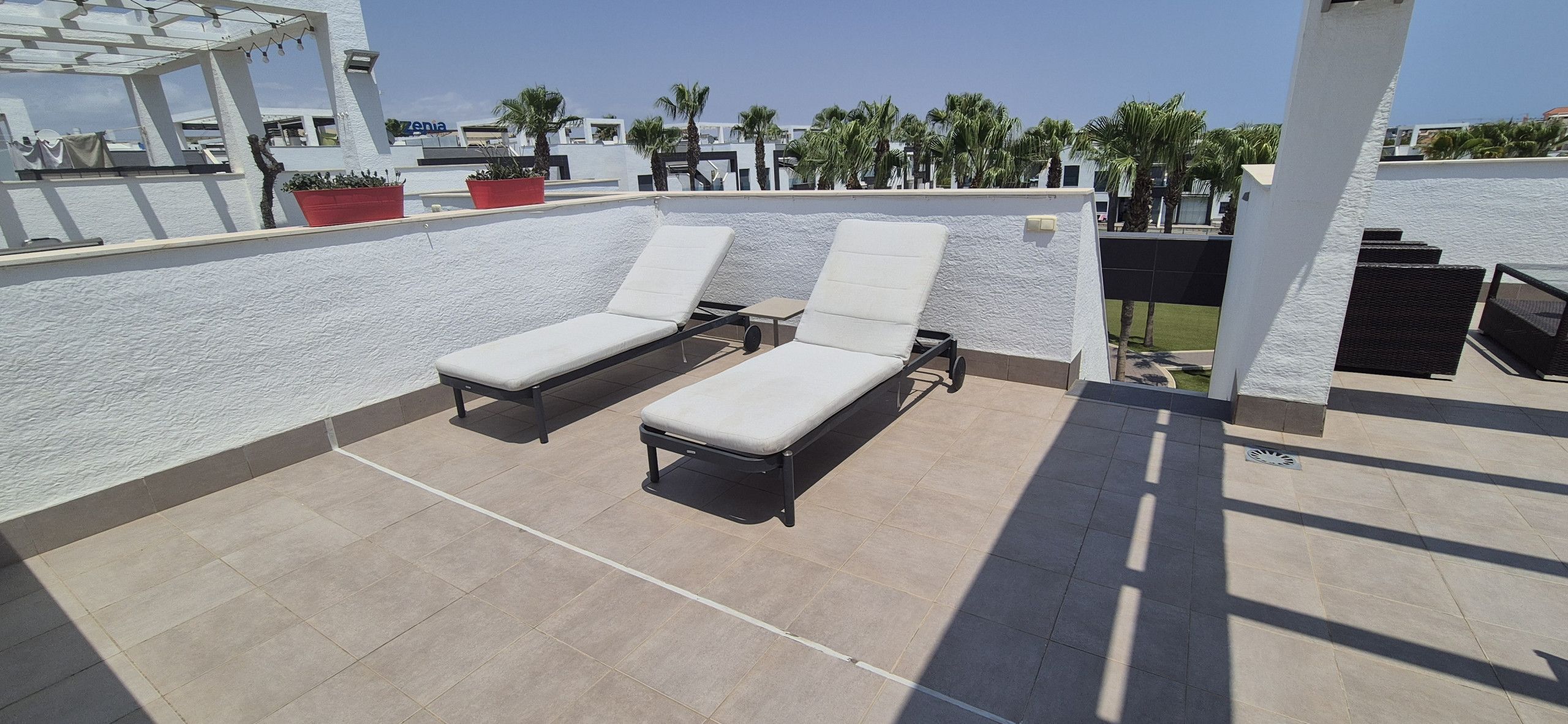 Una terrazza sul tetto con due sdraio, un pergolato e piante in vaso.