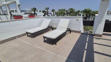 Una terrazza sul tetto con due sdraio, un pergolato e piante in vaso.