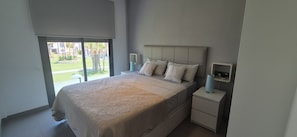 Un dormitorio con una cama grande, una mesita de noche y un ventanal con vistas a un jardín.