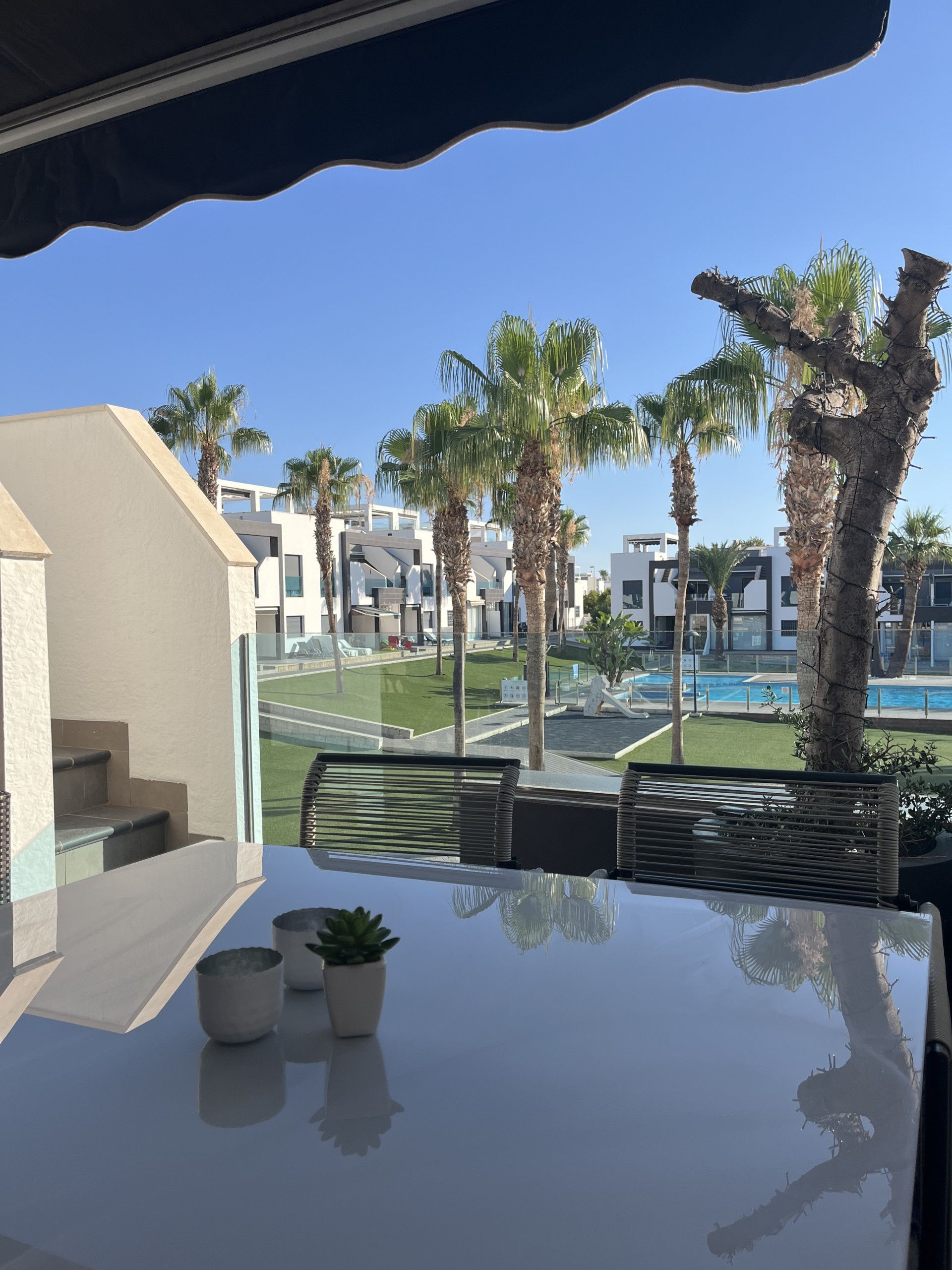 Un balcón con vistas a una piscina, palmeras y edificios modernos.