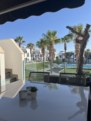 Un balcó amb vista a una piscina, palmeres i edificis moderns.