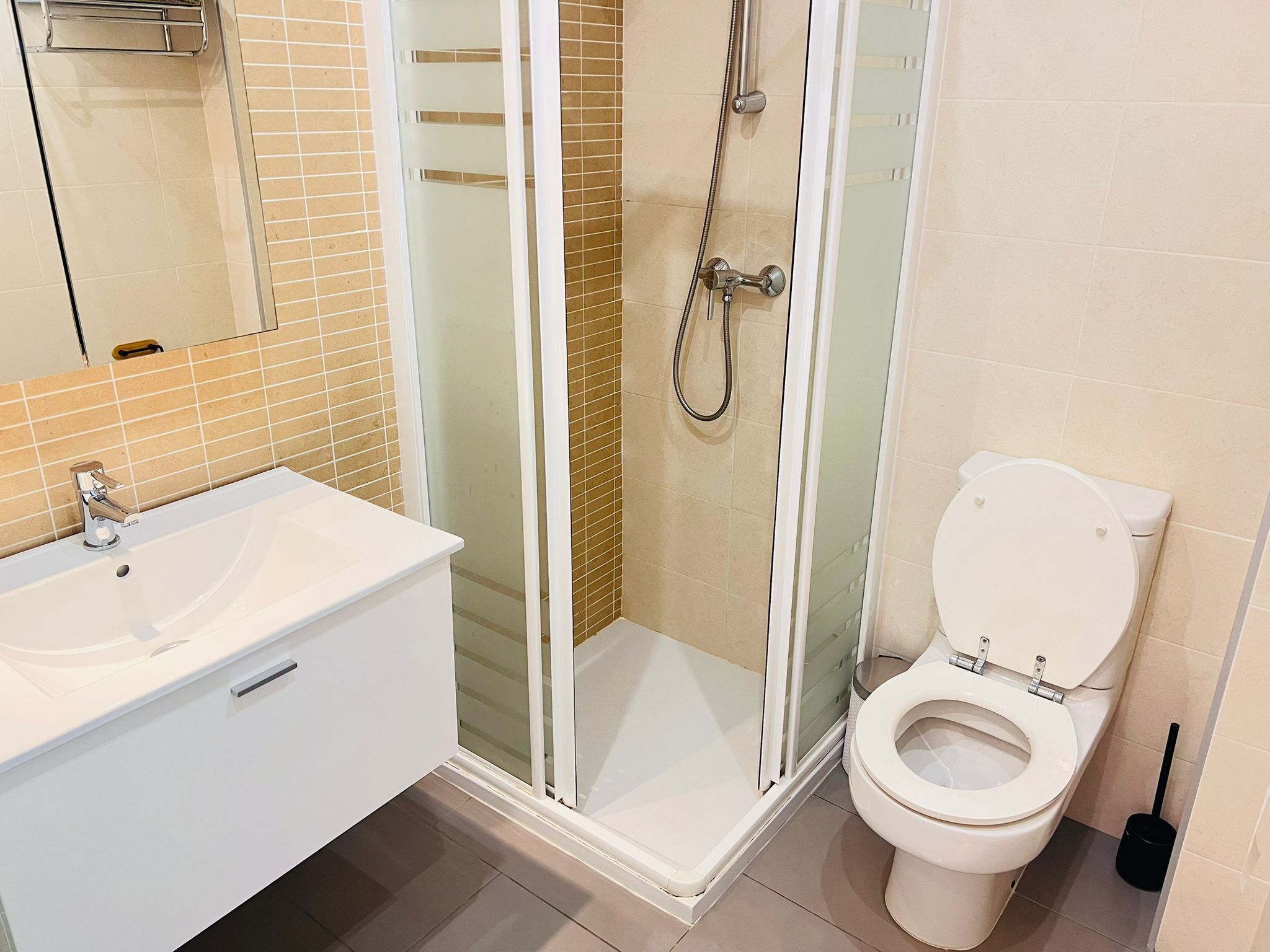 Un baño moderno con lavamanos blanco, inodoro y zona de ducha con mampara de vidrio.
