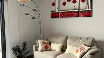 Una sala de estar moderna con un sofá beige, una mesa de centro blanca y una obra de arte colgada en la pared.