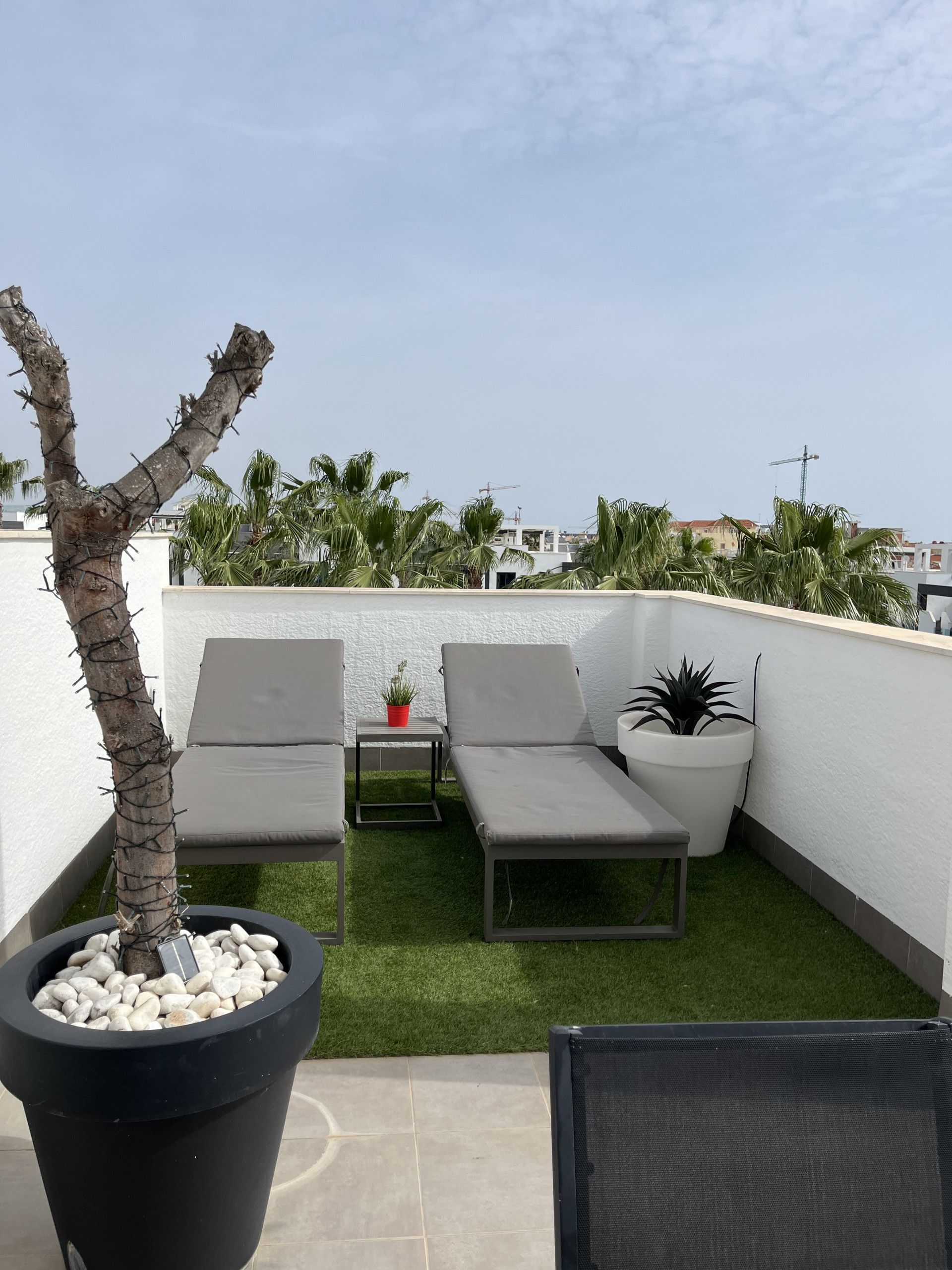 En tagterrasse med to liggestole, et lille bord og plantekrukker.