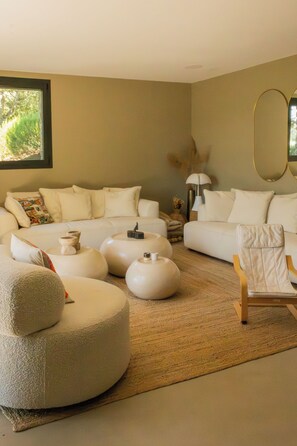 Un salon moderne avec un canapé beige, des poufs ronds, une chaise en bois et un miroir au mur.