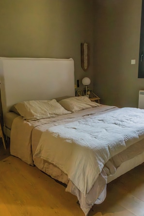 Un dormitorio con cama, mesita de noche, lámpara y un objeto en la pared.