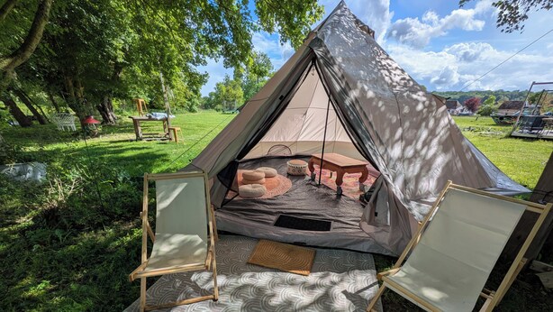 Een tent opgesteld in een grasveld met een tafel en stoelen ervoor.