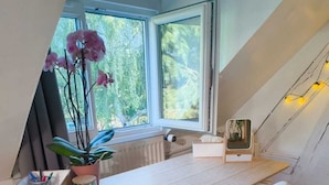 A modern room with a wooden desk, white chair, potted plant, and a window with a view of greenery.