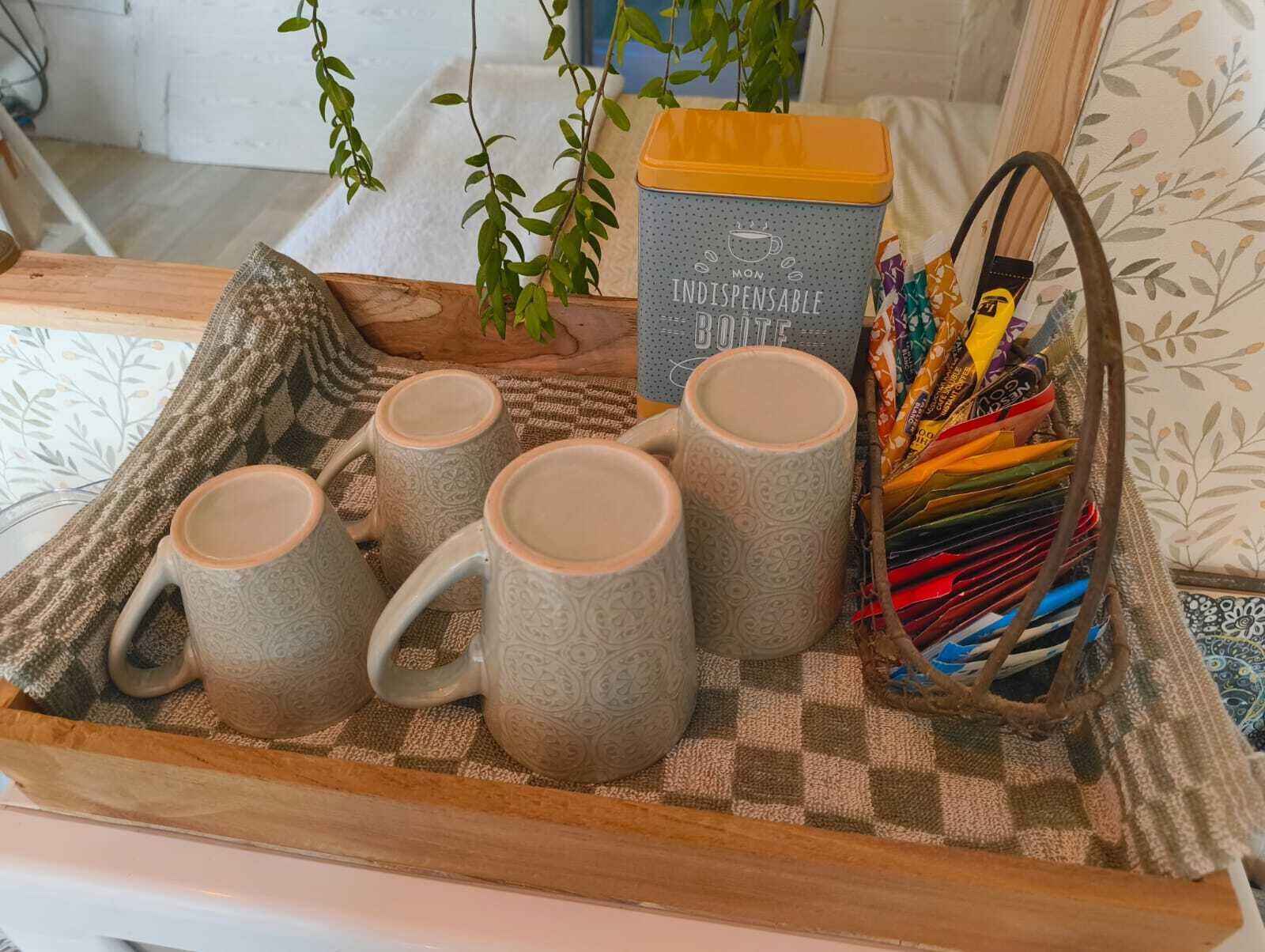 A tray with four grey mugs, a yellow container labeled 'MON INDISPENSABLE BOITE,' and a basket of colorful pencils.